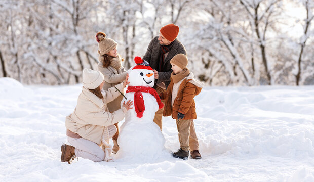 Happy children sculpting funny snowman together with parents in winter snow-covered park