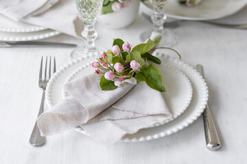 Beautiful table decor for a wedding dinner with a spring blooming apple tree flowers. Celebration of a special event. Fancy white plates, wineglasses