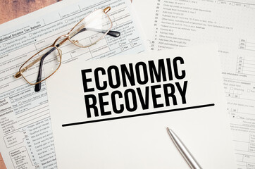 economic recovery words on tax forms and pen on wooden background