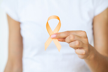 Woman in white t-shirt holding and showing orange awareness ribbon in her hands