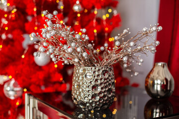 Natural Christmas composition from decorative branches with beads in a vase on background of redchristmas tree. Christmas mood. Stylish composition