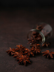 Anise stars scattered from the glass jar on the brown table in the dim light
