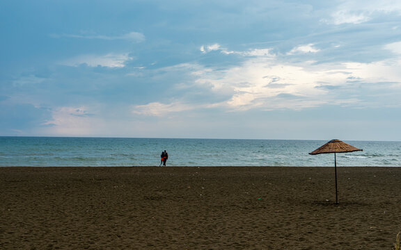 Couple walking and relaxing on sand. Travel vacation background concept on with single wicker umbrella in Samandağ, Antakya. Beautiful scene of beach, sea, blue sky and clouds. Copy space for text.