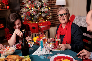 Family christmas celebration, woman and mother sitting at festive dinner table at home party. People eating traditional xmas food, drinking, laughing in decorated place with warm candlelight