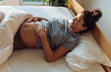 Pregnant woman laying in bed and looking at belly