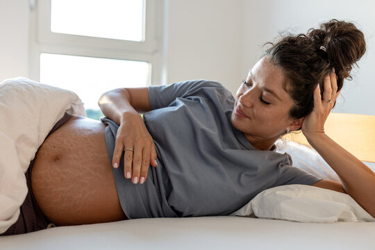 Pregnant woman laying in bed and looking at belly