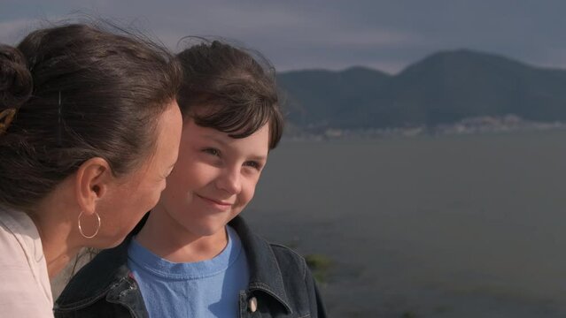 Time with mother against sea. A mother kiss her sad daughter and child smile after on the shore. A concept of happy relations between mother and child by the sea.