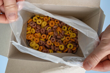 hands open a box of cereal corn rings 