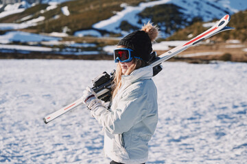 pretty girl equipped with a hat and glasses carries some skis in the snow