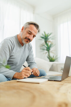 Vertical photo of Bearded mature adult man writing and using laptop