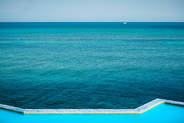 Fototapeta na wymiar Infinity pool next to the ocean on a blue day. View of the edge of an pool next to the sea during daytime