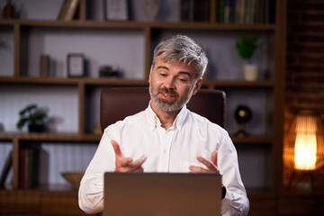 Successful man talking over laptop webcam in virtual chat sitting at workplace. Businessman in...