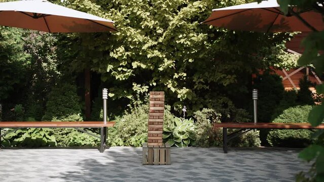 Jenga game tower stands on wooden box in green courtyard of house.