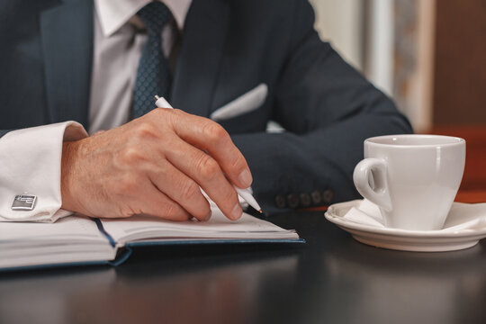 Close up of businessman hands making notes in diary during meeting