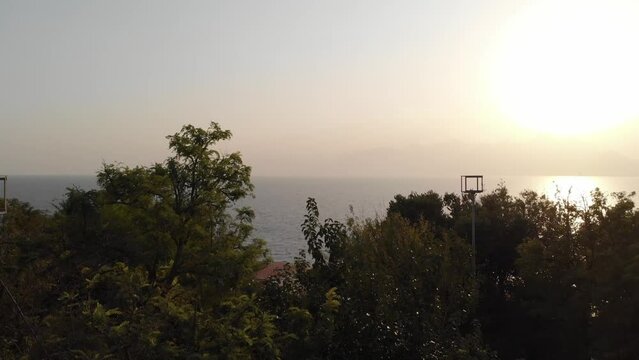 The camera rises above the trees during sunset and offers a view of the sea. High quality 4k footage