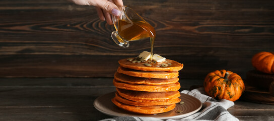 Woman pouring sweet honey onto tasty pumpkin pancakes on plate