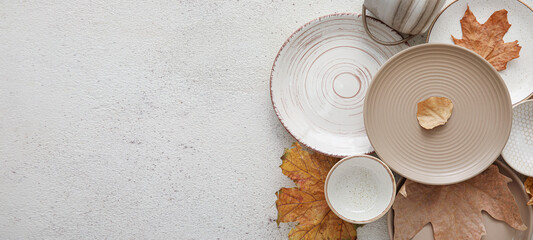 Plates with cup and autumn leaves on white background with space for text