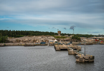 Sweden, Stockholm - July 16, 2022: Port terrain where Mobil tanks and offices replaced by piles of dirt for new ongoing construction. Pier still present under blue morning sky. Green belt