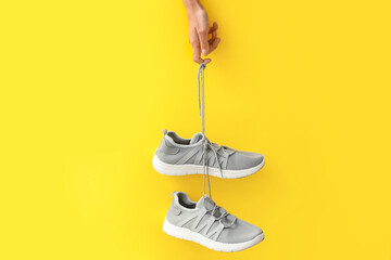 Woman holding grey sneakers on yellow background