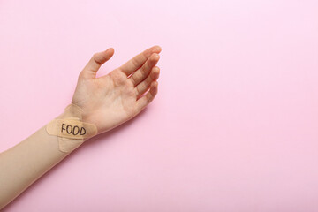 Female hand with plasters and word FOOD on color background. Anorexia concept