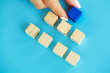Wooden blocks with a human hand placing one cube at the top on blue background.