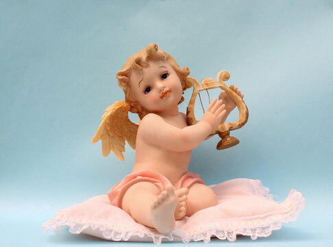 Figura de &Aacute;ngel sentado en coj&iacute;n tocando un arpa.