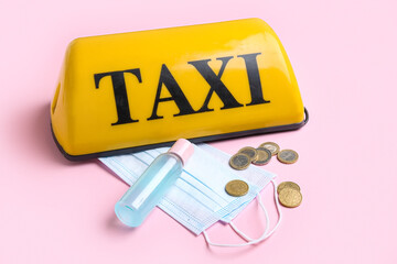 Yellow taxi roof sign, medical masks, coins and sanitizer on pink background
