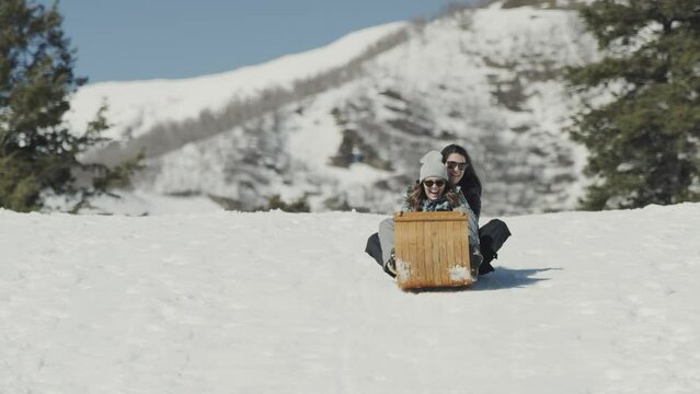 Slow motion of smiling girls riding toboggan on snowy hill / Tibble Fork, Utah, United States