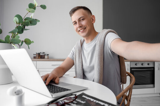 Young man with laptop taking selfie at home