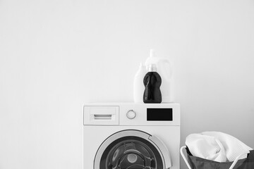 Washing machine with bottles of detergent and folding laundry basket near light wall