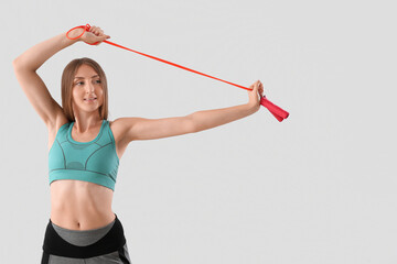 Sporty young woman with jumping rope on light background