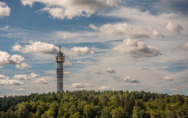 Fototapeta premium Sweden, Stockholm - July 17, 2022: Cookie tower, Kaknästornet, communication and broadcasting tower over green forest under blue cloudscape