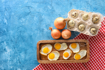 Wooden board with fried quail eggs and onion on color background