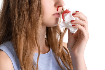 Young woman with nosebleed and tissue on white background, closeup