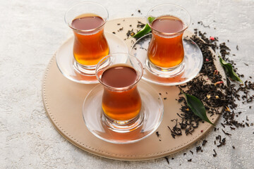 Glass cups of black tea and dried leaves on light background