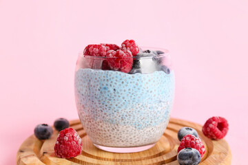 Board with glass of chia pudding and berries on pink background, closeup