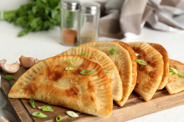 Wooden board with tasty chebureks on light background, closeup