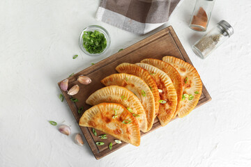 Wooden board with tasty chebureks on light background