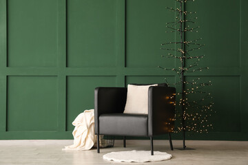 Black armchair, creative Christmas tree and basket with plaid near green wall