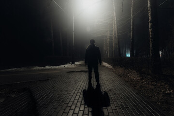 Sad man alone walking along the alley in night foggy park - obrazy, fototapety, plakaty