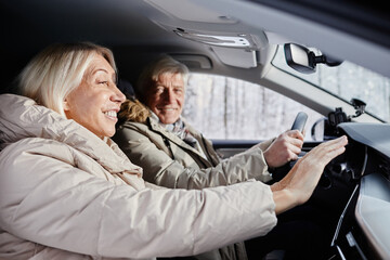 Side view portrait of cheerful senior couple driving car in winter and trying to warm hands on car heater, copy space