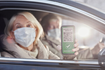 Close up of woman showing digital vaccination code from car window and wearing mask during winter vacation, copy space