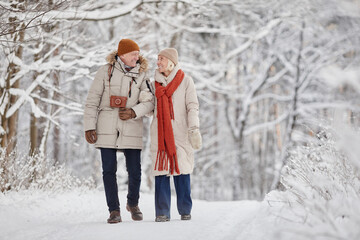Full length portrait of happy senior couple enjoying walk in winter forest and looking at each...