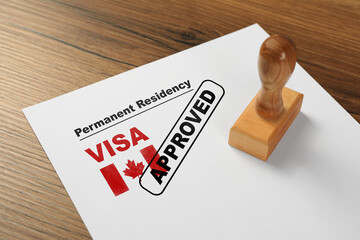 Document with approved permanent residency visa in Canada and stamp on wooden table - obrazy, fototapety, plakaty