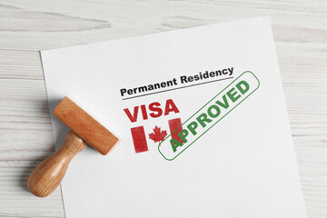 Document with approved permanent residency visa in Canada and stamp on white wooden table, top view