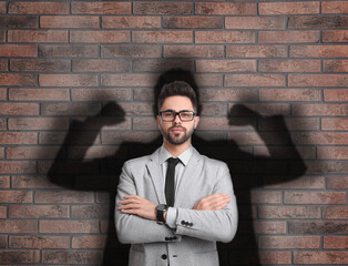Businessman and shadow of strong muscular man behind him on brick wall. Concept of inner strength