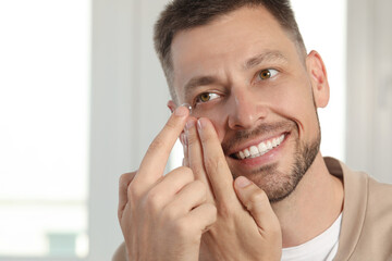 Man putting contact lens in his eye at home, space for text