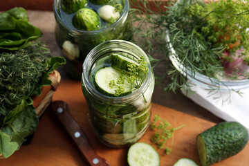 Glass jars, fresh cucumbers and herbs on wooden table. Pickling recipe