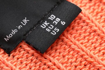 Clothing labels on knitted orange garment, closeup