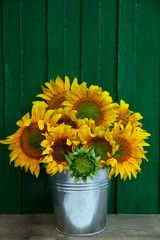 Bouquet of beautiful sunflowers in bucket on wooden table near green wall © New Africa